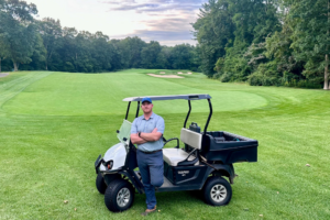 Lake of Isles Director of Agronomy Cody Woods poses against a golf cart on the course.